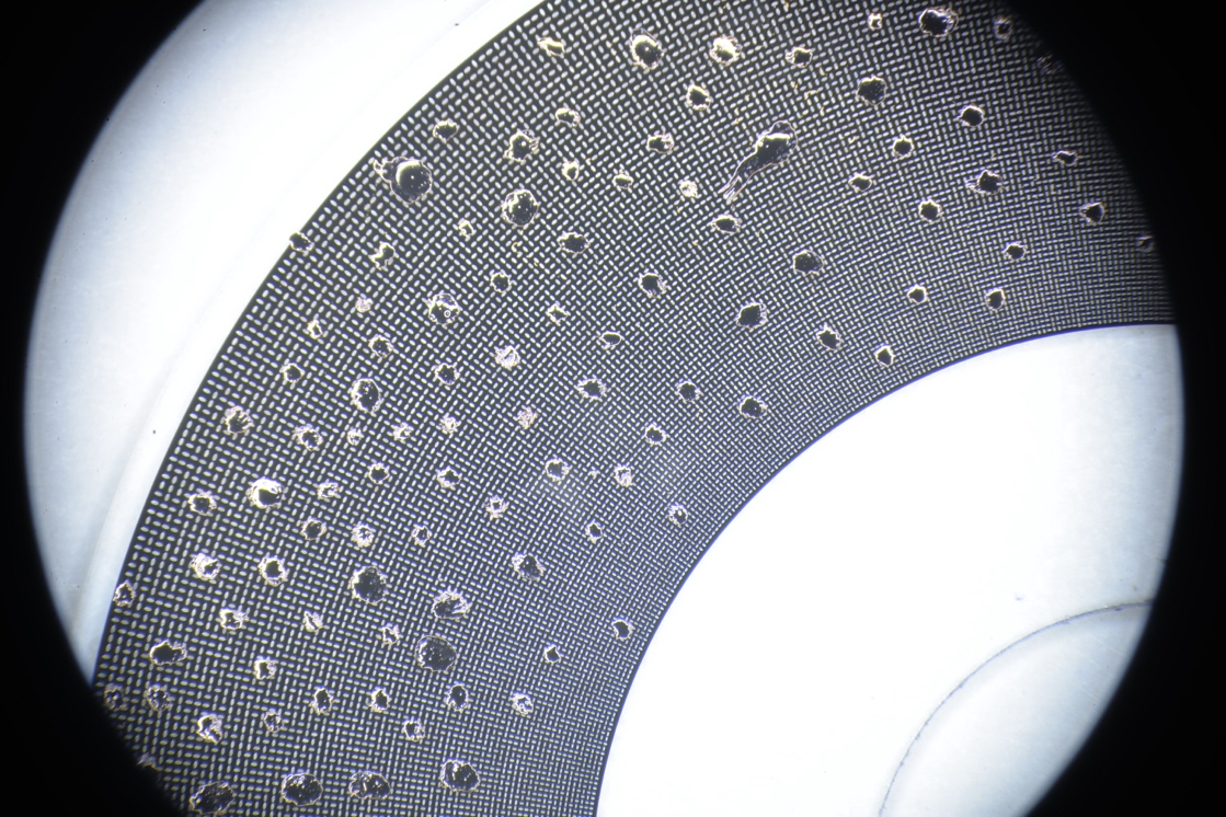 Microscope view of a PreciSen encoder disc covered in dense water and oil droplets, with the 2D code pattern still readable.