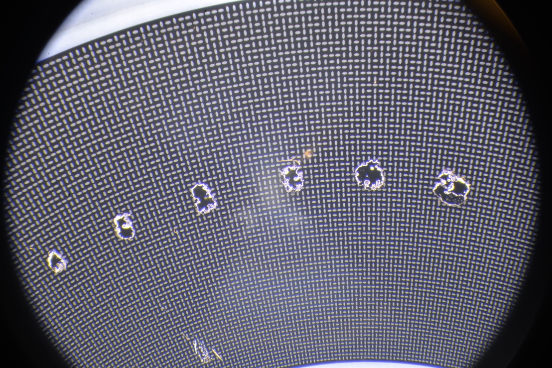 Microscope view of a PreciSen encoder disc with large dark obstructions covering portions of the 2D code pattern.